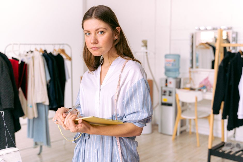 Fashion designer in studio holding notebook, pondering clothing designs.